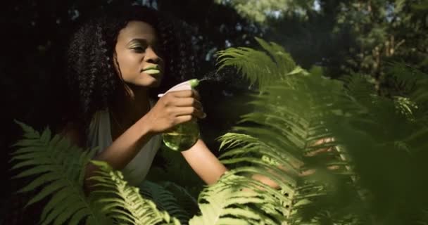 4k. Rápido y en cámara lenta. Rutina del hogar. Naturaleza exótica. Mujer afroamericana con labios y ojos verdes rocía agua en plantas de interior — Vídeo de stock