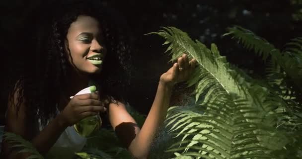4k. Snabba och långsamma rörelser. Hushållsrutin. Exotisk natur. afro amerikansk kvinna med gröna läppar och ögon sprutar vatten på inomhusväxter — Stockvideo