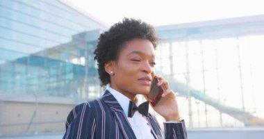 4 bin. Seyahat, digtal, iş. Şık giyinmiş çekici Afrikalı Amerikalı kadın modern cam bir binanın önünde yürürken telefonla konuşuyor.