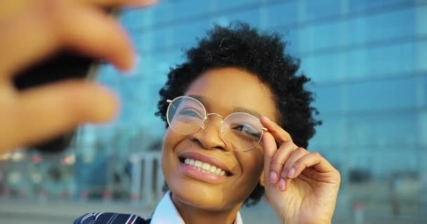 4k. Negocios, estilo de vida, viajes. Emociones positivas. Atractiva mujer afroamericana en traje desnudo con estilo toma una selfie en su teléfono de pie fuera — Vídeos de Stock