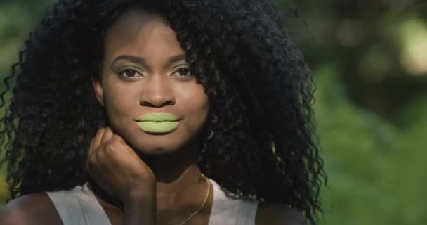 Close up retrato um modelo africano atraente com lábios verdes e cabelos cacheados posando em um fundo de plantas tropicais — Vídeo de Stock