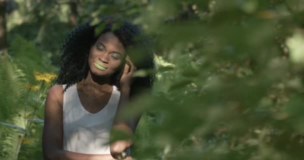 Hermosa modelo africana en vestido blanco con labios verdes posando sobre un fondo de plantas tropicales — Vídeo de stock