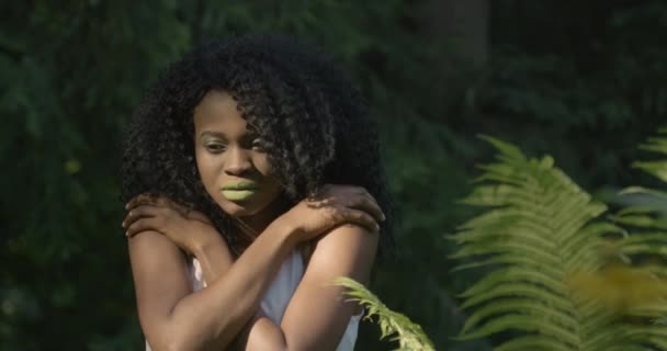 4k. Snabba och långsamma rörelser. Attraktiv afroamerikansk kvinna med gröna ögon och läppar ser rakt in i kameran och ser kall ut stående i exotisk skog — Stockvideo