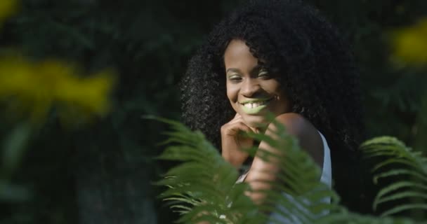 Hermosa joven en verano sonriendo sobre el fondo verde del follaje tropical. Movimiento lento — Vídeo de stock