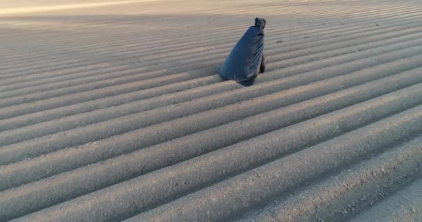 Environmental protection. Death of nature. Apocalypse. Man dressed in black cape walks along the grey field towards the sun. Aerial view — Stock Video