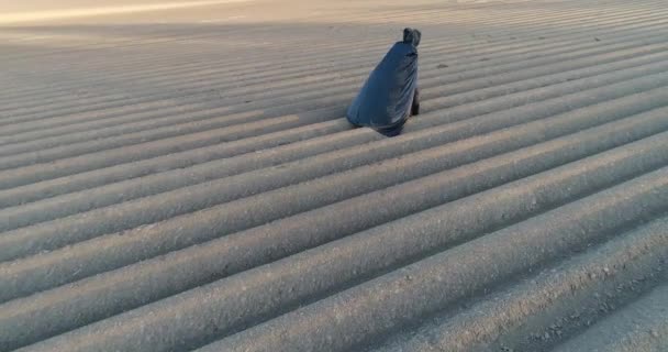 Protección del medio ambiente. Muerte de la naturaleza. Apocalypse. Hombre vestido con capa negra camina a lo largo del campo gris hacia el sol. Vista aérea — Vídeo de stock