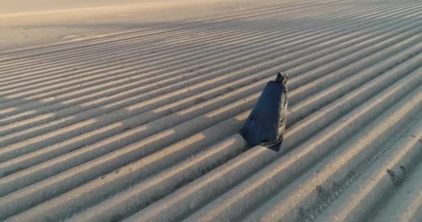 Protección del medio ambiente. Muerte de la naturaleza. Apocalypse. Hombre vestido con capa negra camina a lo largo del campo gris hacia el sol. Vista aérea — Vídeo de stock