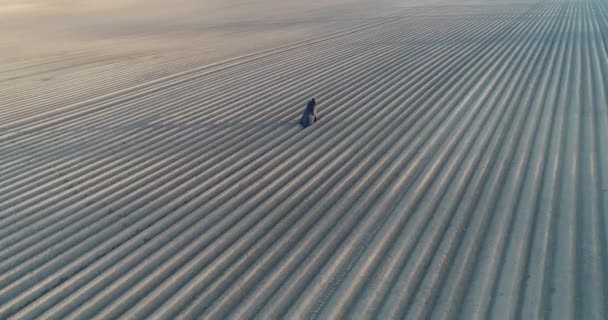 Un uomo in vecchi vestiti con un mantello nero cammina sulla terra nera. Vista dal drone. Malvagio — Video Stock