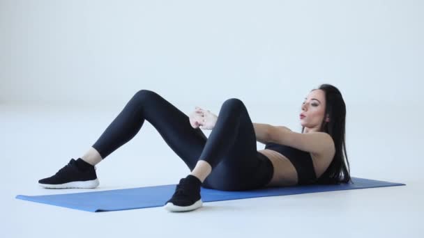 Joven deportista musculosa está haciendo el estiramiento de la parte superior de la espalda y doblarse de rodillas mientras está acostado en la alfombra de ejercicio en el fondo blanco. — Vídeos de Stock