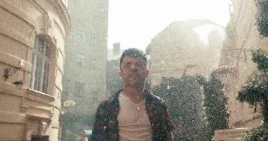 Çekici genç esmer, güneşli bir günde yağmurun keyfini çıkarırken elini kaldırıyor ve bağırıyor..