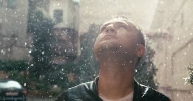 Yakışıklı, rahat adam yağmurda yukarı bakıyor. Güneşli bir gün. Yakın plan portre. 4k görüntü.