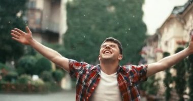 Duygusal, neşeli, günlük kıyafetleri olan bir adam sokaklarda yağmur yağarken elini kaldırıp bağırıyor. 4k görüntü.
