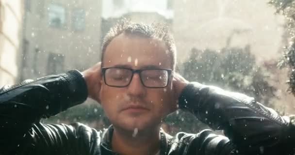 Close-up retrato do homem bonito com óculos desfrutando da chuva durante o dia ensolarado. — Vídeo de Stock