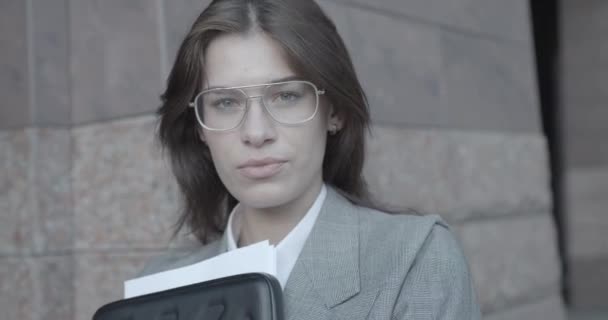 Rotierende Kamera um die selbstbewusste hübsche Geschäftsfrau mit Brille, die in die Kamera blickt. Sie hält den Aktenstapel in der Hand. 4k. — Stockvideo