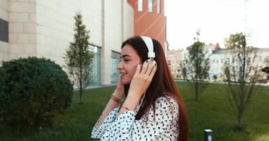 Kulaklıkla müzik dinleyen ve cadde boyunca yürüyen mutlu esmer kadının portresi. 4k görüntü.