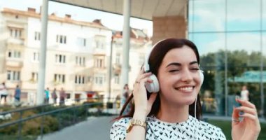 Neşeli kızın portresi. Kulaklıklarıyla müzik dinlerken sokakta yürüyüp dans eden..
