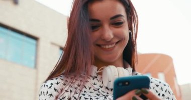 Çekici bir genç esmer ve büyüleyici bir gülümsemesi var. Cep telefonuyla geziniyor ve mesajlaşıyor. Yakın plan portre. 4k görüntü.