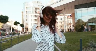 Güzel gülüşlü neşeli esmer bayan dışarıda beyaz kulaklıklarla dans ediyor. 4k görüntü.