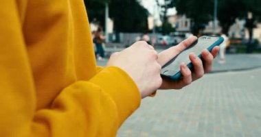 Kimliği belirsiz erkeklerin sarı kazak giyip dışarıdaki cep telefonuna mesaj atarken ve göz atarken yakın görüntüsü. 4k görüntü.