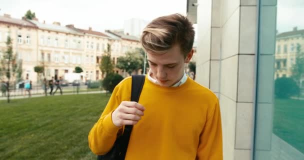 Портрет молодого блондина в жёлтом свитере, идущего по улице и трогающего его волосы. 4k кадров. — стоковое видео