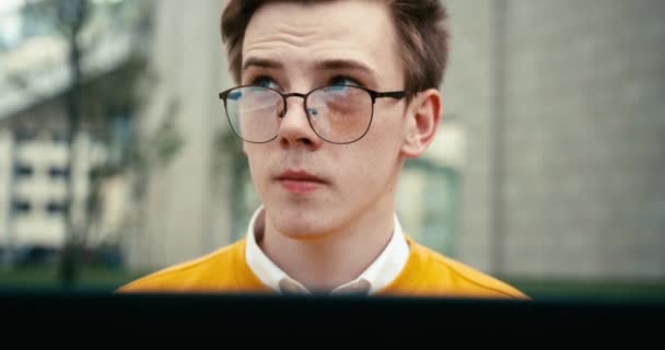 Retrato fechado do tipo pensativo confiante jovem em óculos que trabalham no computador portátil. Filmagem 4k. — Vídeo de Stock