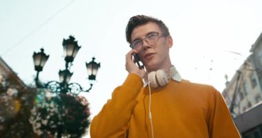 Gözlüklü genç çekici adamın portresi caddedeki cep telefonuyla mutlu bir şekilde konuşuyor. 4k görüntü.