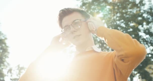 Portretul tânărului adolescent blond adorabil în ochelari care se bucură de muzică în căști pe strada însorită. 4k imagini . — Videoclip de stoc
