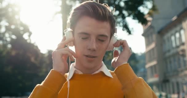 Portret van de knappe hipster met blond haar die geniet van de muziek in zijn koptelefoon. Hij draagt de gele trui. 4k-beelden. — Stockvideo