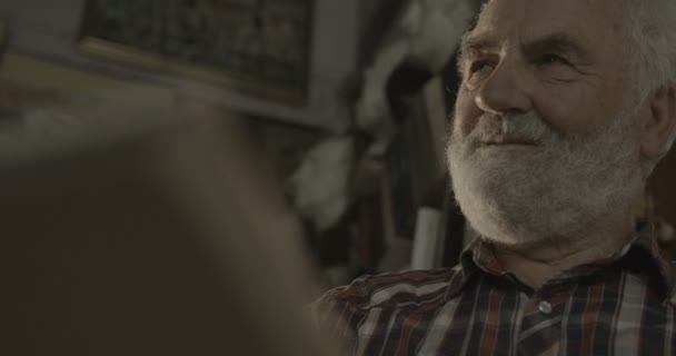 Zbliżenie portret starego artysty z szarą brodą rysujący obraz w jego warsztacie. Materiał 4k. — Wideo stockowe