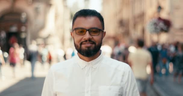 Charming handsome afro-american man with eyeglasses is happily smiling at the blurred background of the city. Close-up portrait. — Stock Video