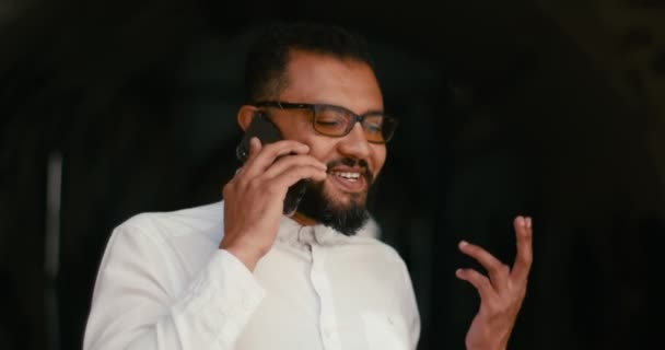 Portrait du beau jeune homme africain parlant joyeusement sur le téléphone portable à l'arrière-plan noir. — Video