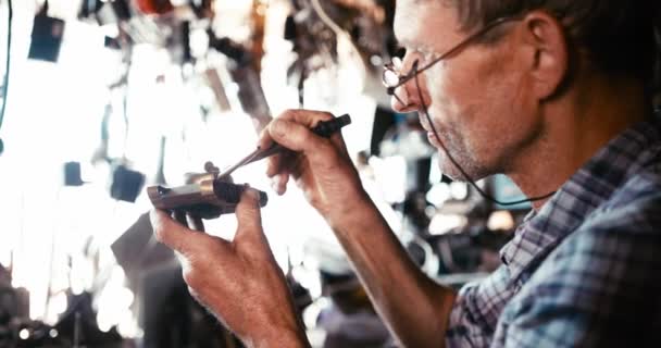 El anciano con gafas está soldando el tanque de hierro en su taller. Captura de cámara ROJA. — Vídeo de stock