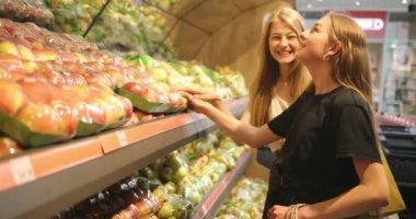 Süpermarkette elma seçen iki güzel kızın portresi. İki genç kadın mandıra ürünleri seçiyor, sebze, markette meyve. 4K video
