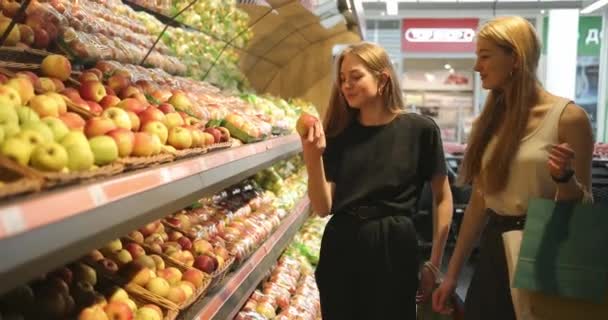 Portret dwóch ładnych dziewczyn, które wybierają jabłka w supermarkecie. Dwie młode kobiety wybierające nabiał, warzywa, owoce w supermarkecie. Wideo 4K — Wideo stockowe