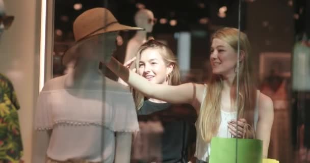 Portrait of two young and pretty women trying on a hat from the mannequin. Two satisfied attractive female shoppers talking after shopping trip. 4K video — Stock Video