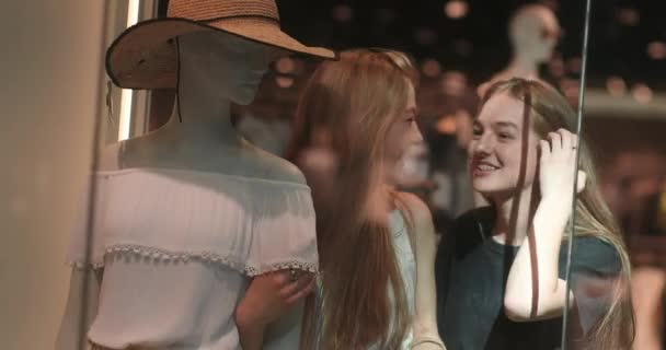 Porträt von zwei jungen und hübschen Frauen, die einen Hut von der Schaufensterpuppe anprobieren. Zwei zufriedene attraktive Käuferinnen unterhalten sich nach dem Einkauf. 4K-Video — Stockvideo