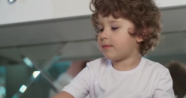 Szczęśliwy poranek w domu. Mały chłopiec bawiący się z rodzicami we wnętrzu kuchni. Położyli rękę na dłoni i podnieśli ją. Biała, przytulna kuchnia i spokojna rodzinna atmosfera. Wideo 4K — Wideo stockowe