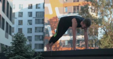 Spor giyimli genç adam balkonda yoga yapıyor. Vücudun gürlemesine yardımcı olmak için yoga egzersizi yapıyor. 4K video