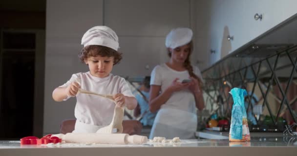 Portrait of little boy who breaks the dough. Young mother is cooking in the kitchen with her son, dirty hands, make the dough for baking. 4K video — Stock Video