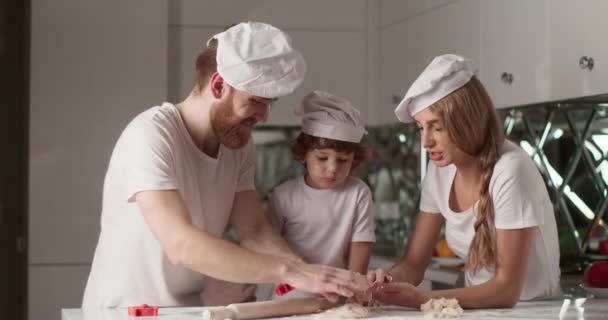 Potret keluarga muda yang tersenyum sedang memasak di dapur. Mereka berlutut adonan dan mengolesi satu sama lain wajah dengan tepung. Dapur yang nyaman dan suasana keluarga yang tenang. Video 4K — Stok Video