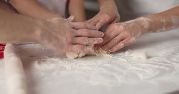 Feche o retrato de mãos arrumadas e como eles amassam a massa. Família jovem está cozinhando na cozinha. Cozinha acolhedora branca e ambiente familiar calmo. Vídeo 4K — Vídeo de Stock