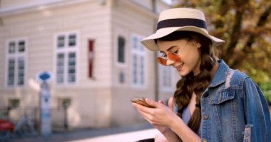 Parlak gün ışığında çekici genç bir kadın şehir merkezinde telefon yürüyüşü yapar. Etrafına bakar. Gülümse..