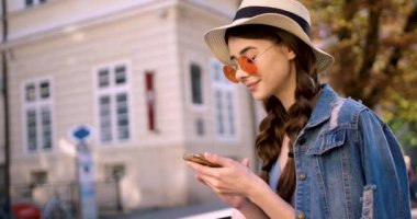 Pembe gözlüklü genç kadın şehir merkezinde akıllı telefon kullanıyor..