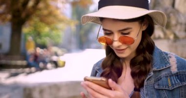 Parlak güneş ışığı altında çekici genç bir kadın şehir merkezinde telefon yürüyüşü yapar saçlarını okşar mutlu yaz internet işleri teknolojinin dışında..