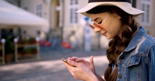Jovem mulher em uma jaqueta de ganga e óculos redondos rosa usam smartphon e sorrindo. — Vídeo de Stock