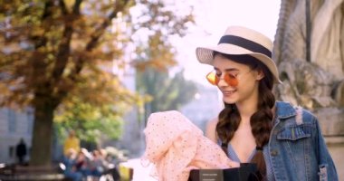 Kot ceketli, pembe yuvarlak gözlüklü ve hasır şapkalı genç bir kadın alışveriş çantasından çıkmış gibi görünüyor.