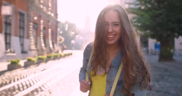 Menina sorridente feliz em camisa amarela, jaqueta jeans azul e mochila amarela corre no centro da cidade — Vídeo de Stock