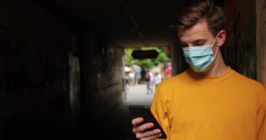 Tıbbi maskeli kızıl saçlı bir adam tünelin yanında durup telefonu kullanıyor. Pandemik koruma