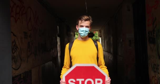 Facet w ochronnej masce medycznej stoi z czerwonym znakiem STOP. Zatrzymać koronawirus — Wideo stockowe