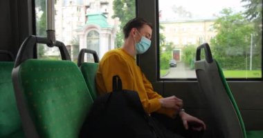 Kızıl saçlı çekici bir adam toplu taşıma araçlarına biniyor. Koruyucu maskeli ve sarı kazaklı genç bir adam tramvayda oturuyor.